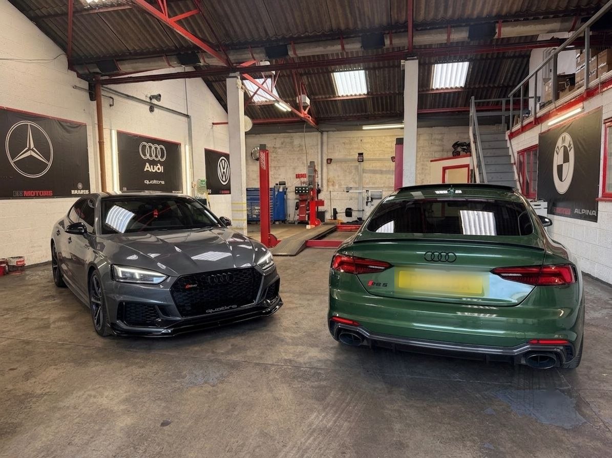 Two Audi RS5s in the EE Motors workshop, with Mercedes, Audi, VW and BMW signage on the walls